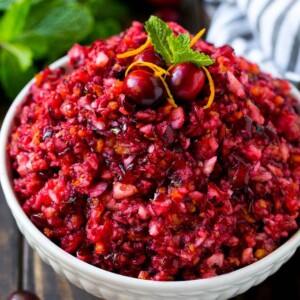 A bowl of cranberry relish topped with whole cranberries, orange zest and mint.