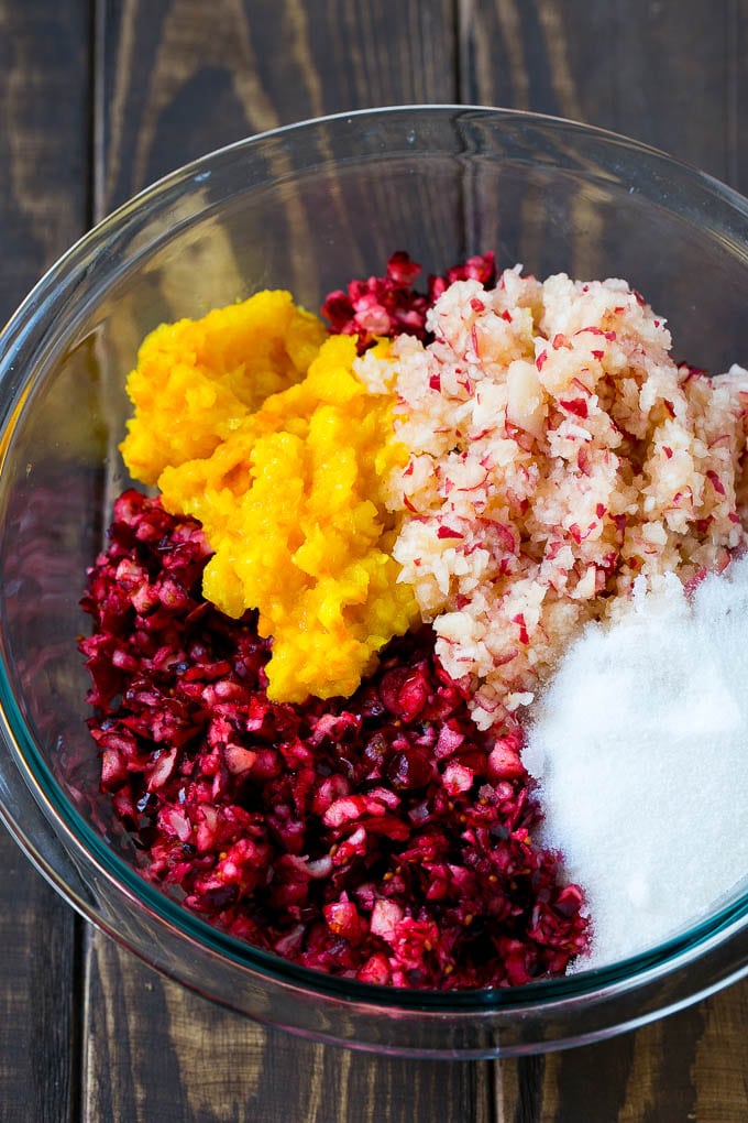 Chopped cranberries, apple and orange with sugar in a mixing bowl.