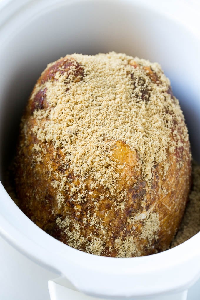 A ham in a crock pot coated with brown sugar.