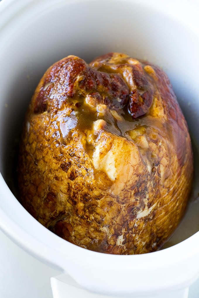 A ham in a slow cooker covered in brown sugar, maple syrup and pineapple juice.