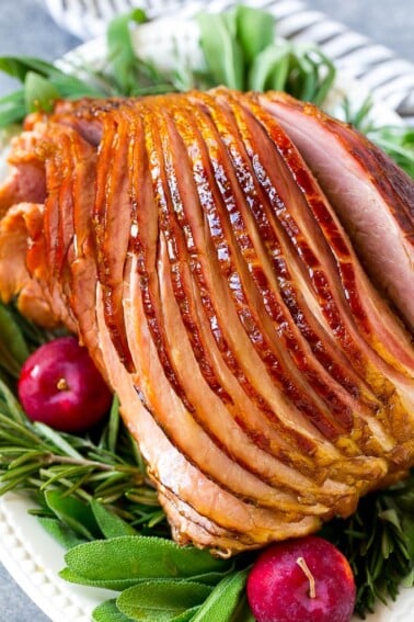 A crock pot ham on a serving plate with herbs and apples for garnish.