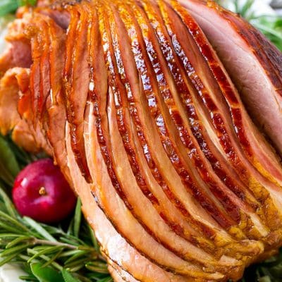 A crock pot ham on a serving plate with herbs and apples for garnish.