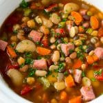 A slow cooker full of ham and bean soup made with vegetables, dried beans and diced ham.