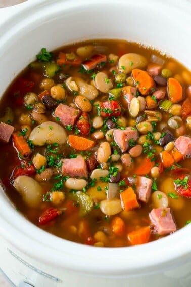A slow cooker full of ham and bean soup made with vegetables, dried beans and diced ham.