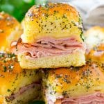A stack of ham and cheese sliders topped with poppy seed butter and parsley.