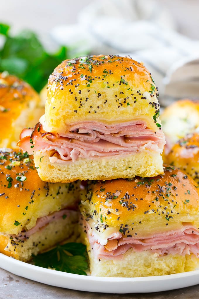 A stack of ham and cheese sliders topped with poppy seed butter and parsley.