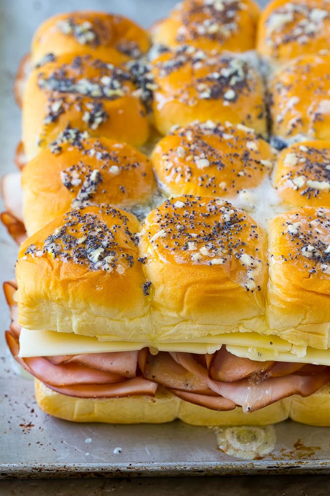 A package of slider rolls topped with ham, cheese and an onion poppy seed butter.