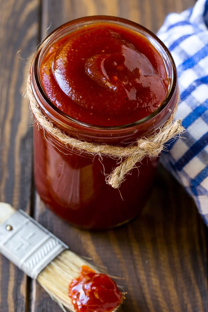 A jar of homemade BBQ sauce with a basting brush near it.