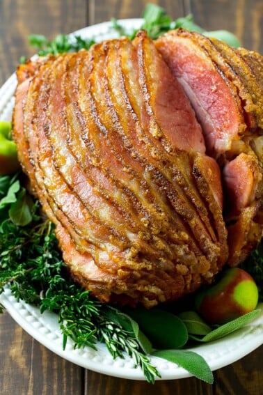 A spiral cut honey baked ham on a serving platter garnished with fresh herbs.