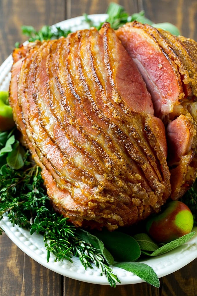 Un prosciutto cotto al miele tagliato a spirale su un piatto da portata guarnito con erbe fresche.