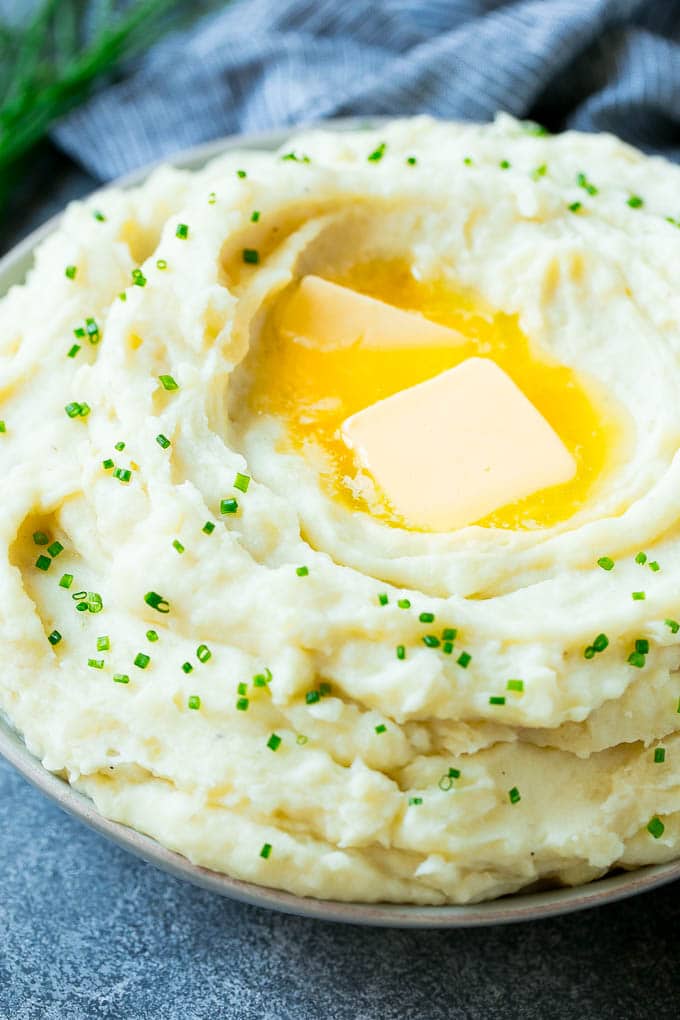 A bowl of fluffy Instant Pot mashed potatoes topped with pats of butter and sliced chives.