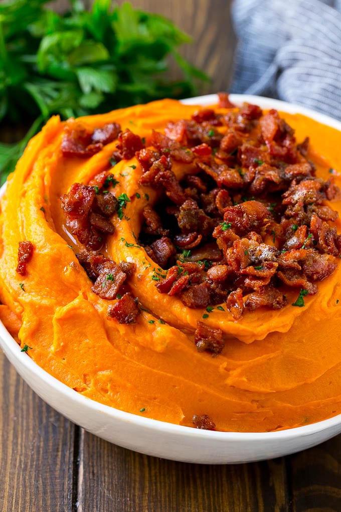 A bowl of smashed sweet potatoes topped with candied bacon.