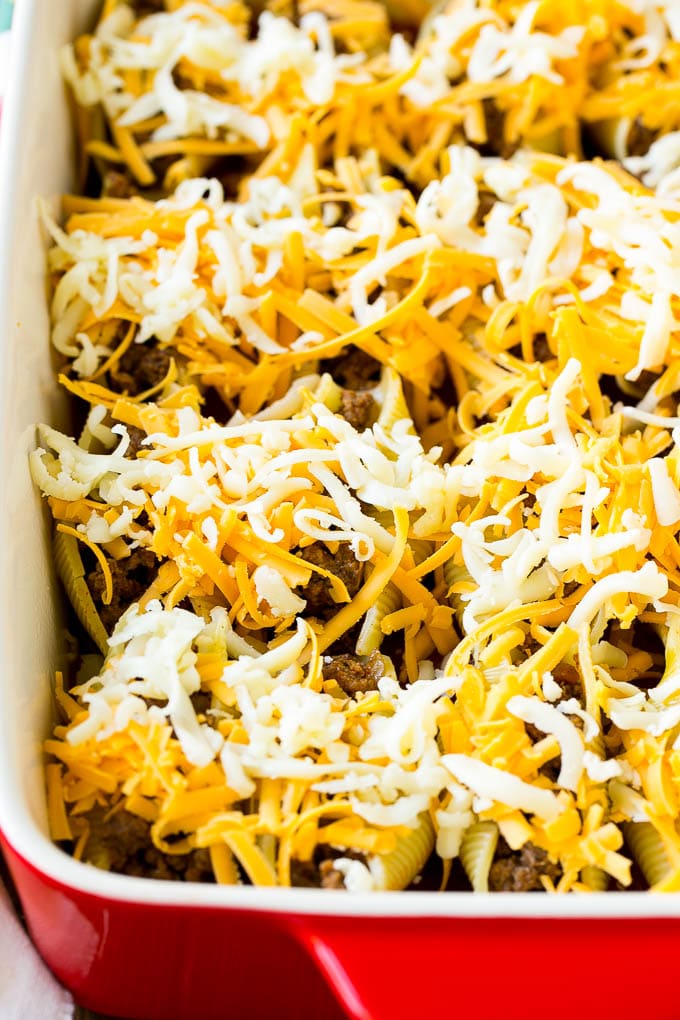 Unbaked Mexican stuffed shells topped with shredded cheese.