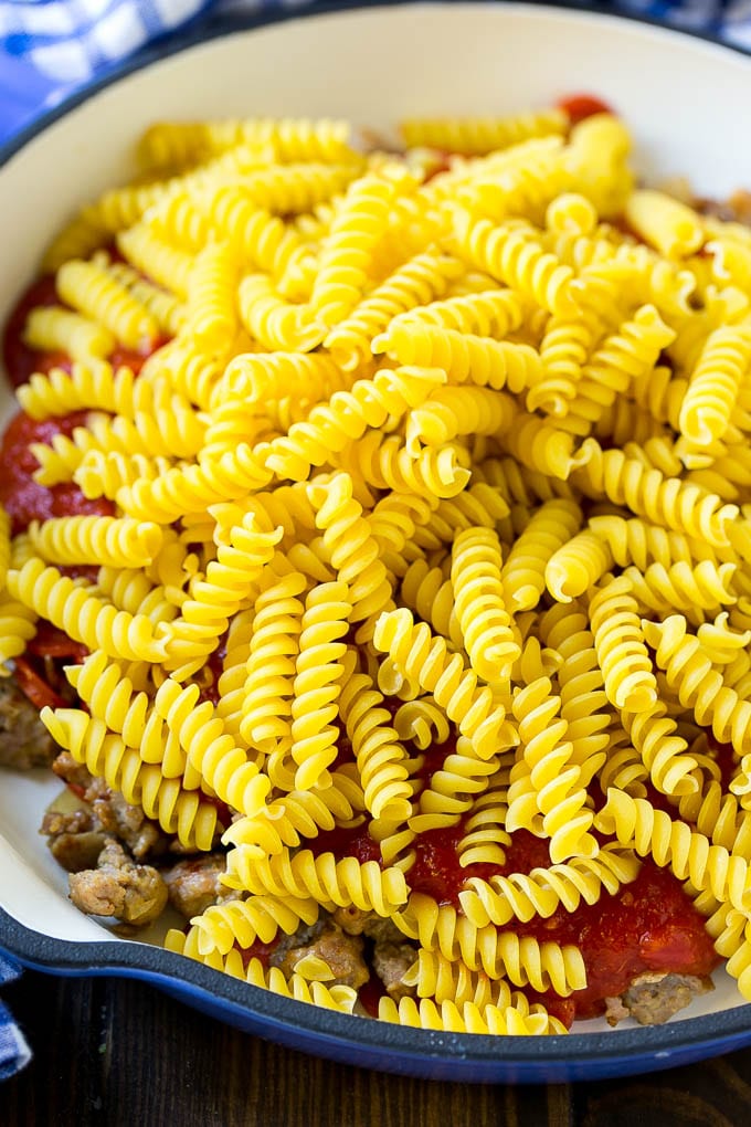 Pepperoni, sausage, tomato sauce and uncooked pasta in a skillet.