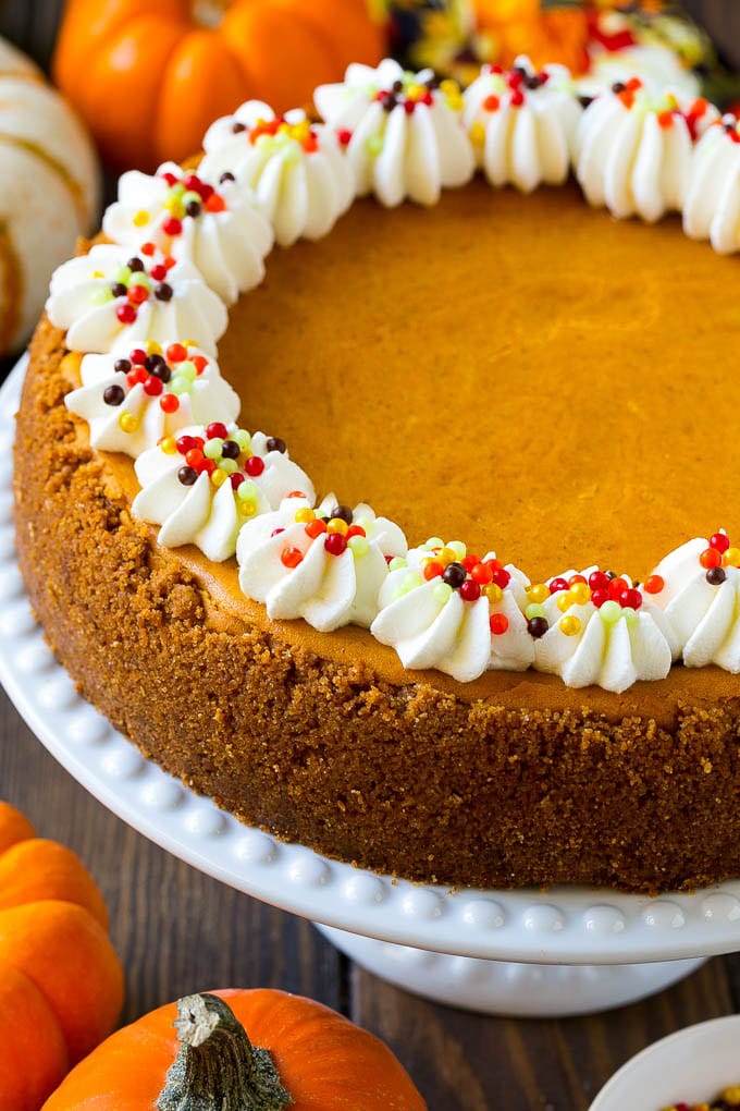 A pumpkin cheesecake on a cake stand topped with whipped cream and sprinkles.