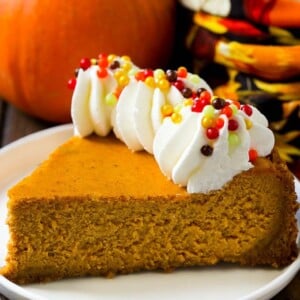 A slice of pumpkin cheesecake on a graham cracker crust, topped with whipped cream and sprinkles.