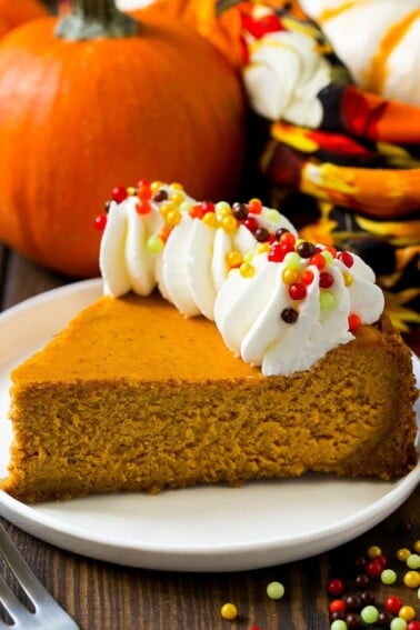 A slice of pumpkin cheesecake on a graham cracker crust, topped with whipped cream and sprinkles.