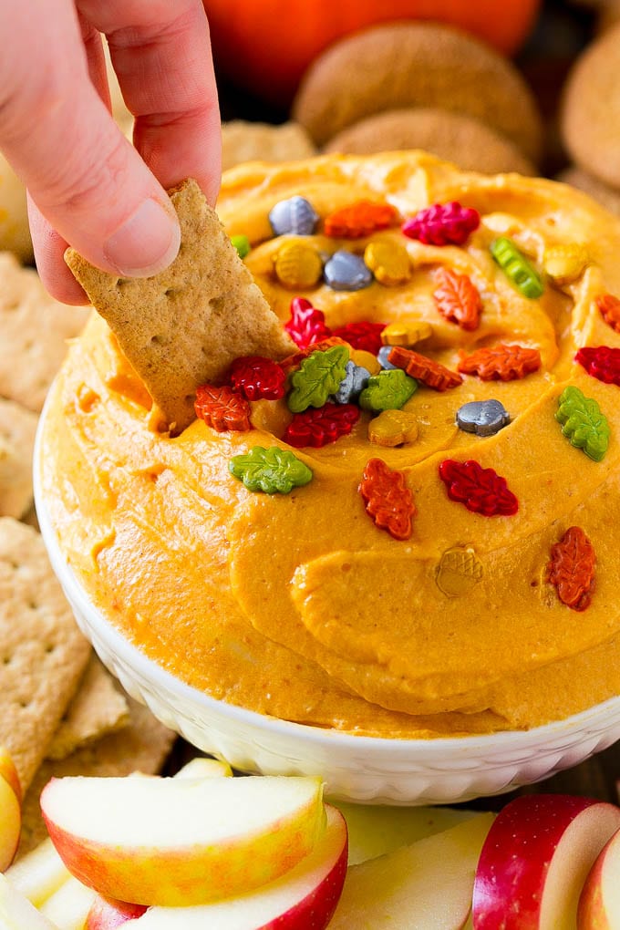 A bowl of pumpkin dip with a graham cracker scooping some out.