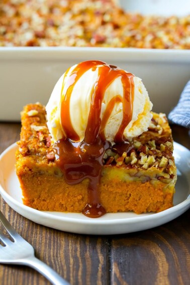 A slice of pumpkin dump cake topped with ice cream and caramel sauce.