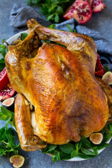 A Thanksgiving roast turkey on a serving platter garnished with herbs, pomegranate and figs.