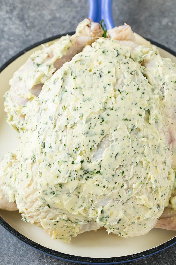 A raw whole chicken coated in garlic and herb butter.
