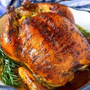 A roasted chicken in a pan garnished with fresh rosemary sprigs.