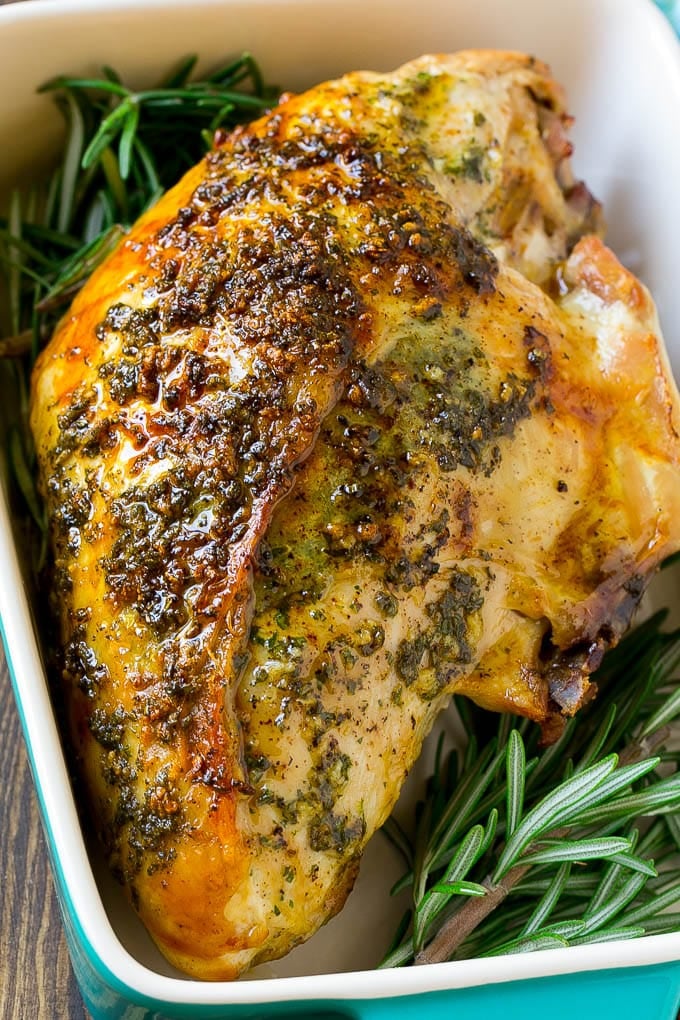Garlic and herb roasted turkey breast in a baking dish with a rosemary garnish.