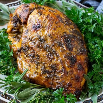 A slow cooker turkey breast on a serving platter with fresh herbs.