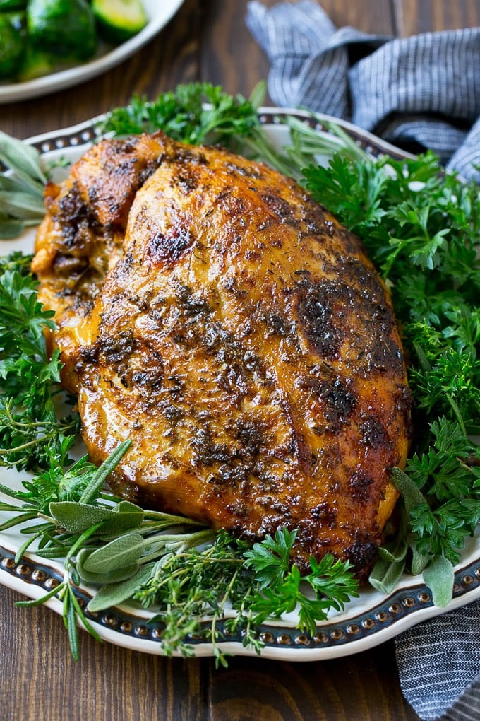 A slow cooker turkey breast on a serving platter with fresh herbs.