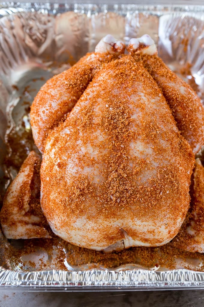 A raw chicken coated with homemade spice rub in a roasting pan.