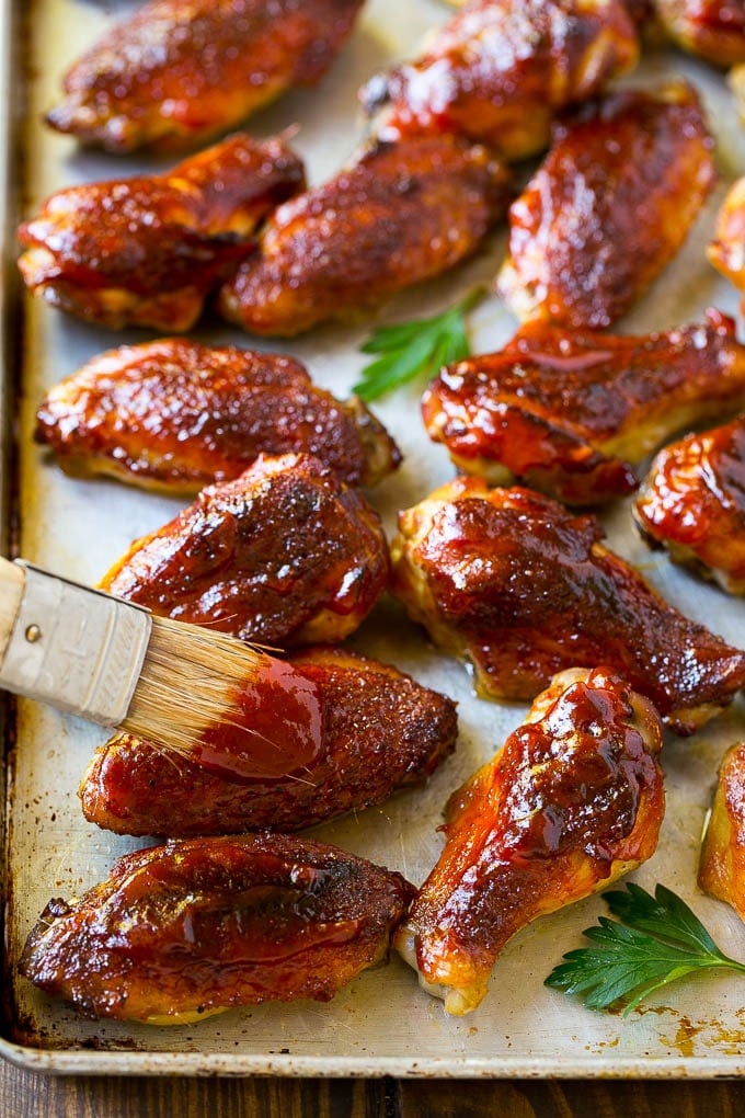 BBQ sauce brushed onto a sheet pan of smoked chicken wings.