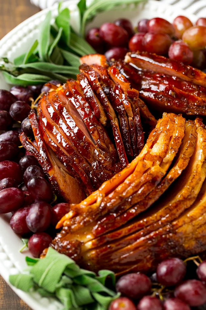 Sliced smoked ham on a serving platter, garnished with grapes and fresh herbs.