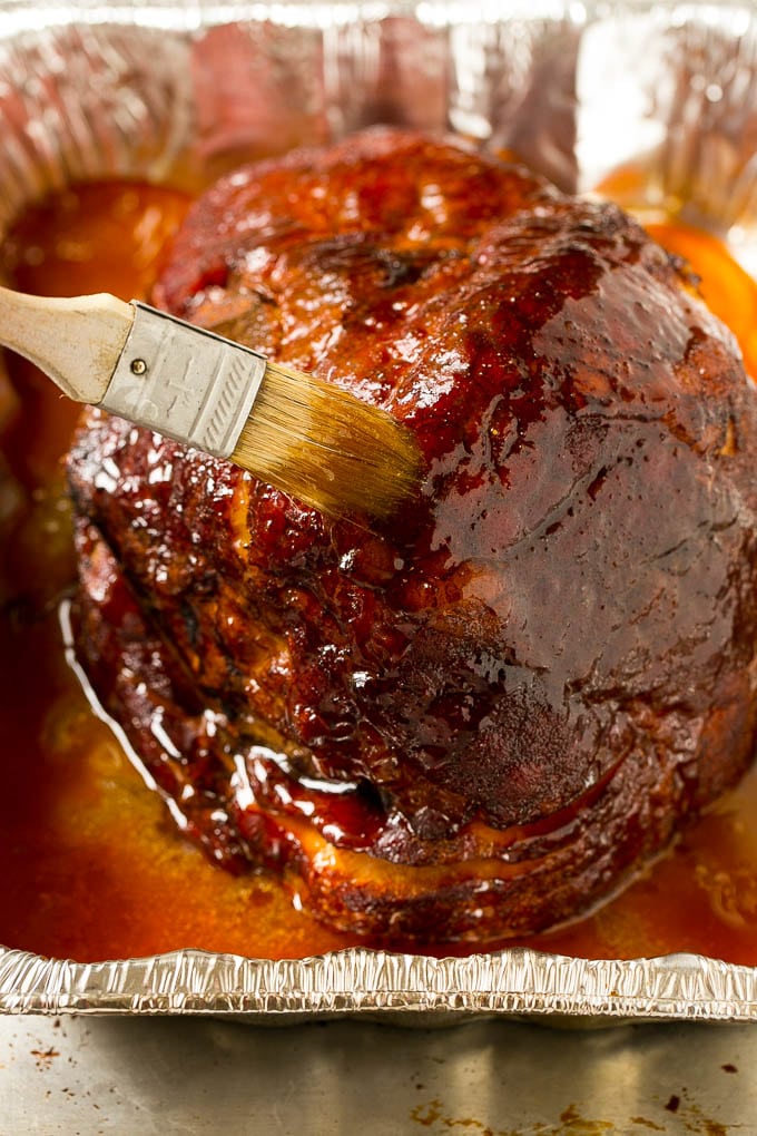 A smoked ham being coated in brown sugar glaze.