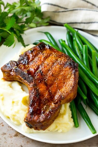 Smoked pork chops over mashed potatoes with green beans on the side.