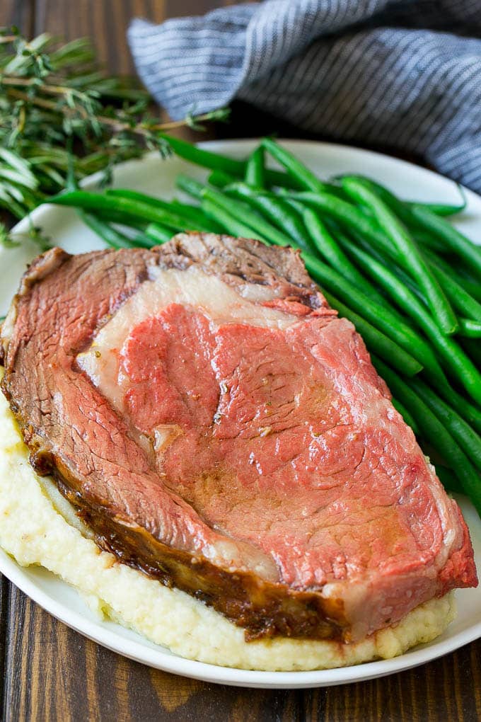 A slice of prime rib over mashed potatoes with green beans on the side.