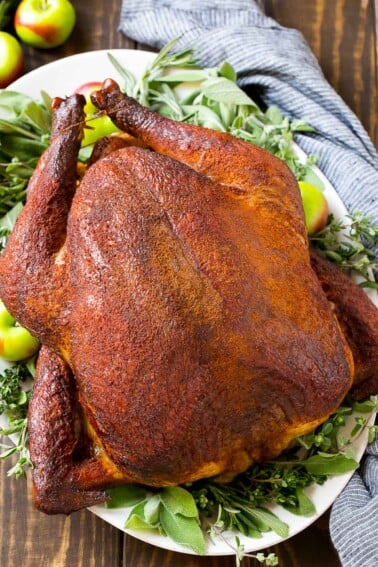 Smoked turkey on a platter garnished with herbs and apples.