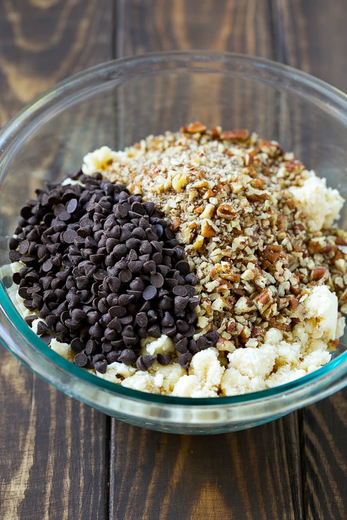 A bowl of cookie dough topped with miniature chocolate chips and chopped pecans.