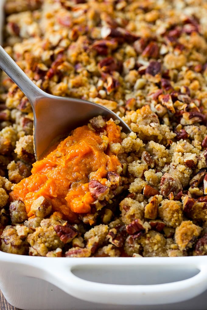 A dish of sweet potato casserole with pecans with a serving spoon in it.