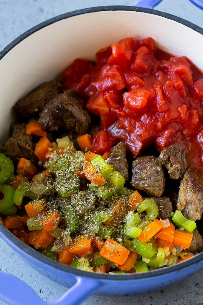 Stew meat, veggies, tomatoes and herbs in a pot.