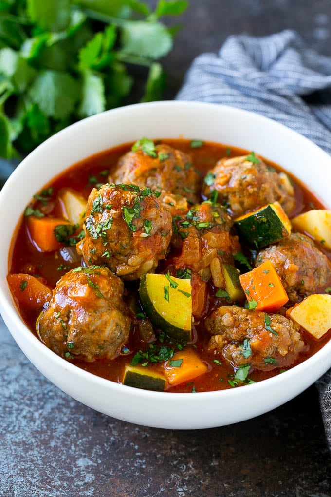 A bowl of albondigas soup with meatballs, carrots, zucchini and tomatoes.