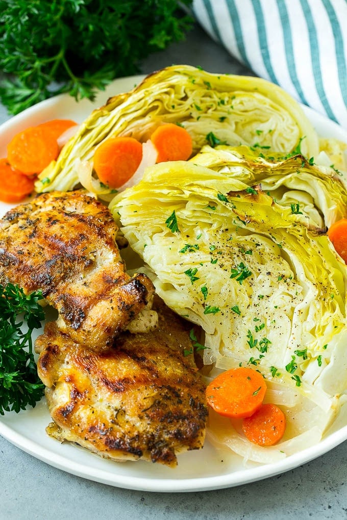 A plate of grilled chicken along with braised cabbage, carrots and onions.
