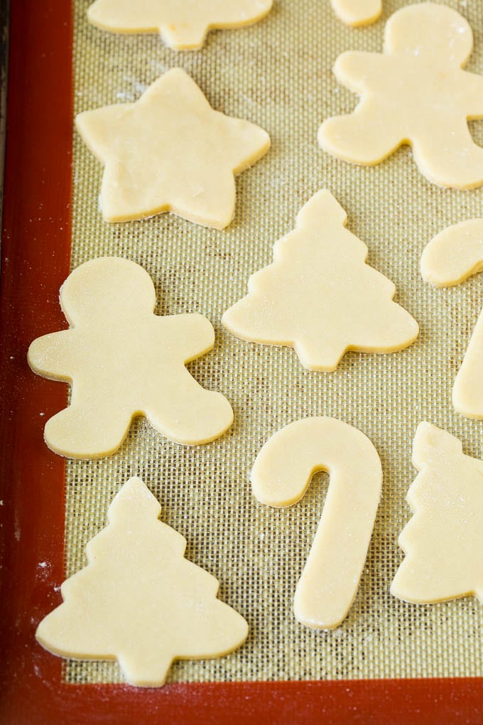 Cookie dough cut into holiday shapes on a baking sheet.