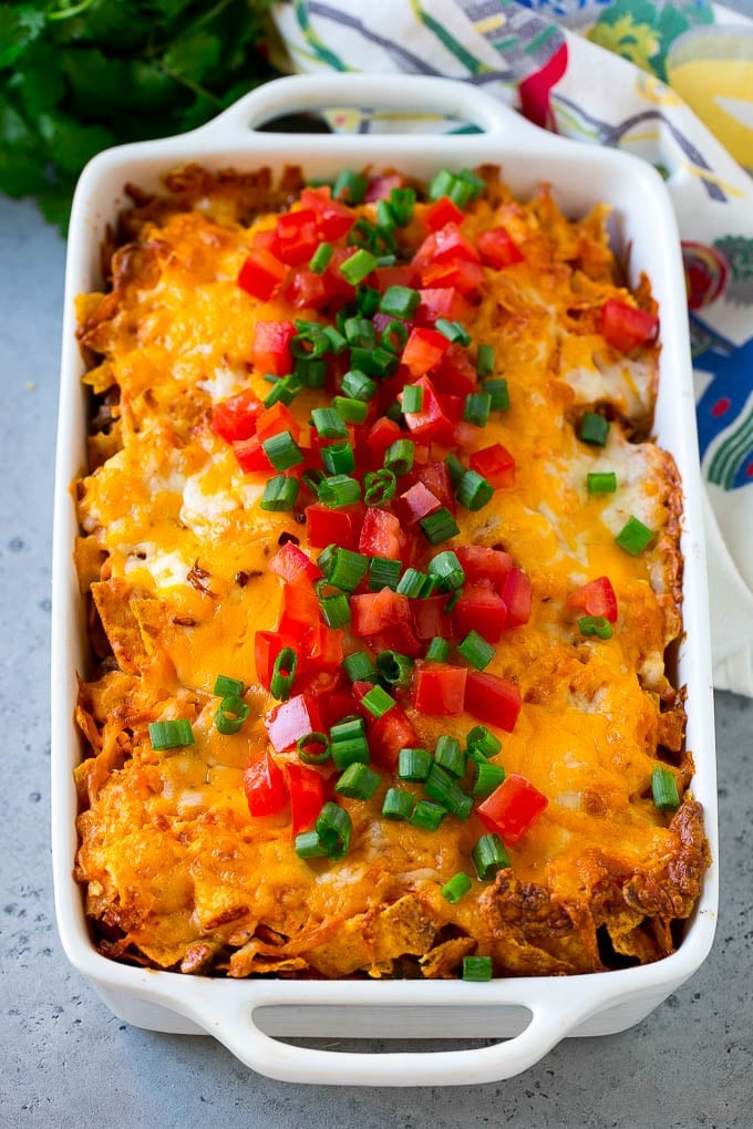 Dorito casserole topped with melted cheese, diced tomatoes and sliced green onions.