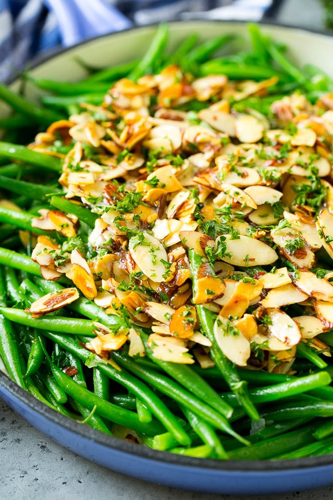 A pan of green beans almondine topped with toasted sliced almonds, butter and chopped parsley.