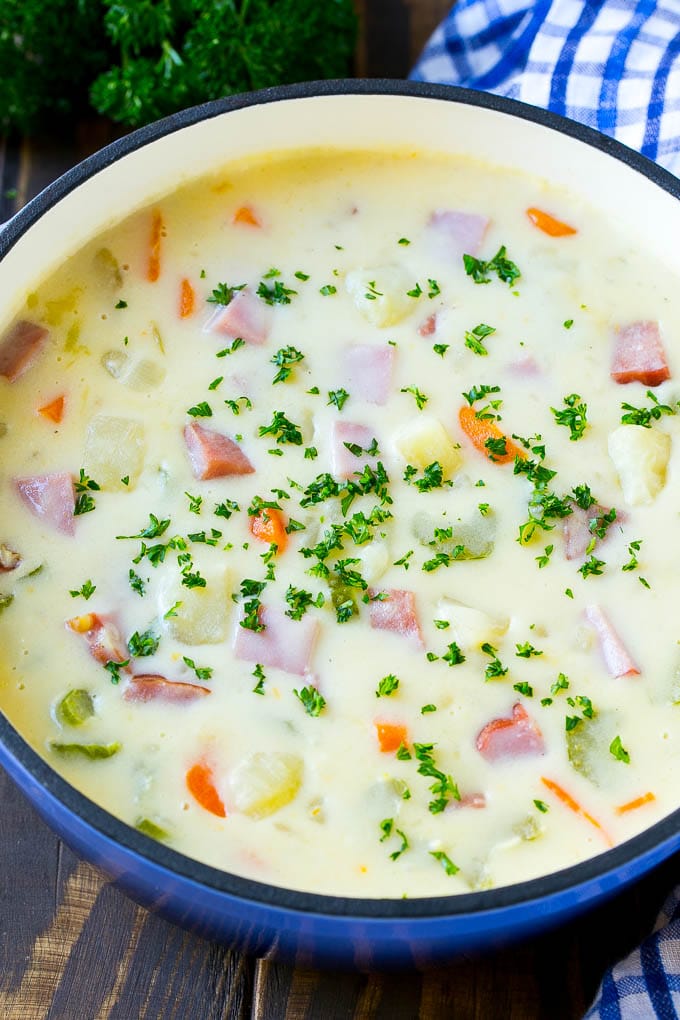 A pot of ham and potato soup with vegetables in a creamy broth, topped with parsley.