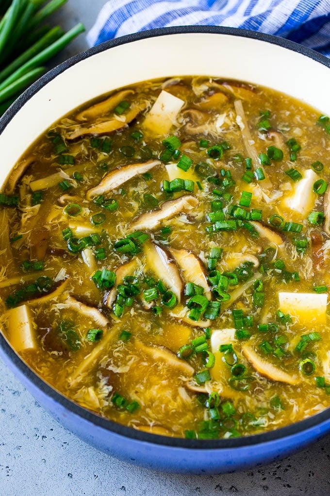 A pot of homemade hot and sour soup with shiitake mushrooms, tofu, bamboo shoots, egg strands and green onion.