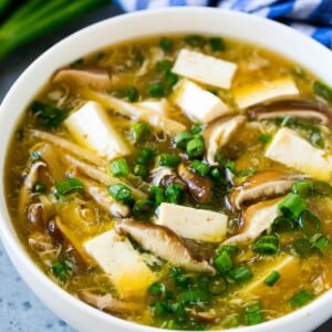 A bowl of hot and sour soup filled with tofu, mushrooms, egg, bamboo shoots and green onion.