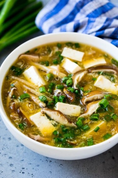 A bowl of hot and sour soup filled with tofu, mushrooms, egg, bamboo shoots and green onion.