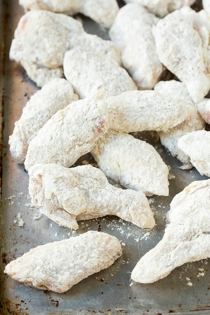 Chicken wings coated in seasoned flour on a baking sheet.