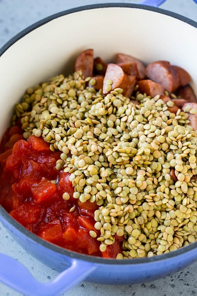 Sausage, vegetables, dried lentils and tomatoes in a pot.